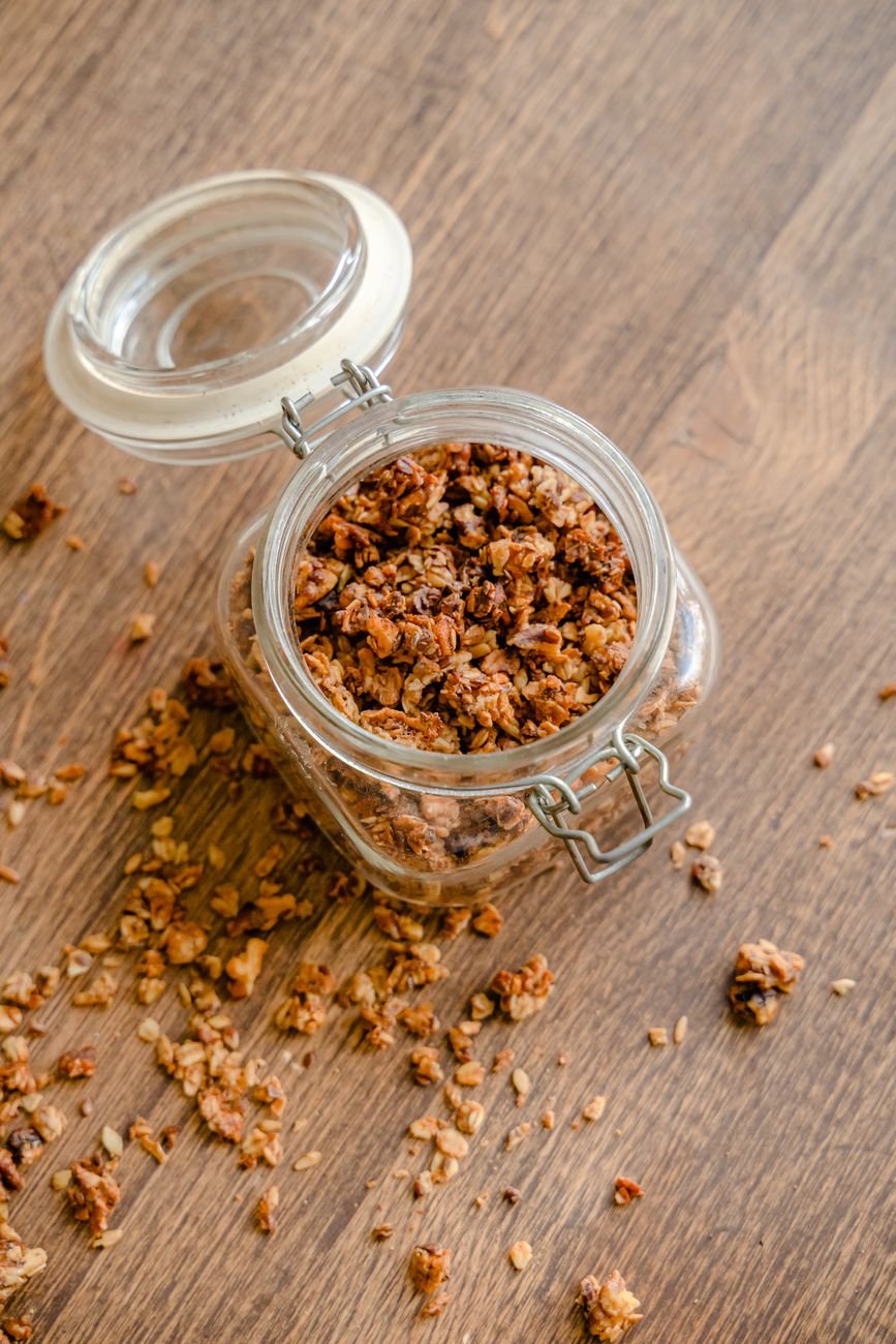 Granola casera cayendo de un frasco abierto sobre una mesa de madera.